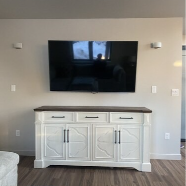 A large TV mounted on a light-colored wall above a white cabinet with a dark brown top.