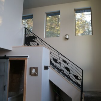 Staircase with black metal railing featuring bear and fish silhouettes; windows in the background.