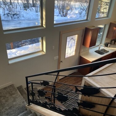 Staircase with fish-shaped railing leads to a door and kitchen; snow visible through windows.