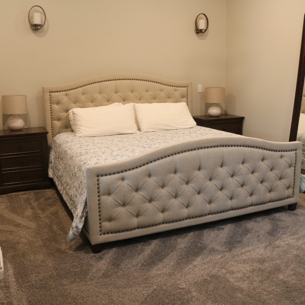 Bedroom with upholstered bed, nightstands, lamps, and a full-length mirror, carpeted floor.
