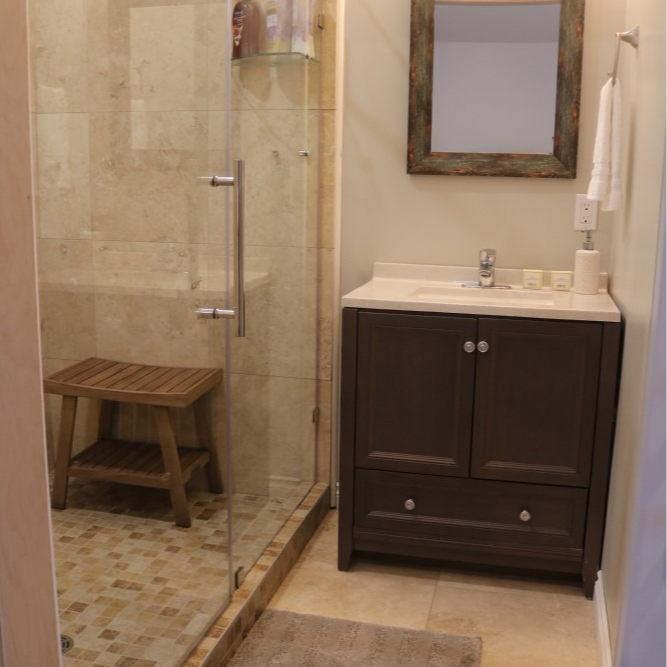 Bathroom with glass shower, wooden stool, brown vanity, and framed mirror.