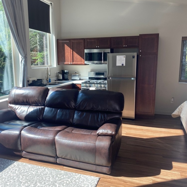 Living space with brown leather recliner, kitchen with stainless steel appliances, and wood flooring.
