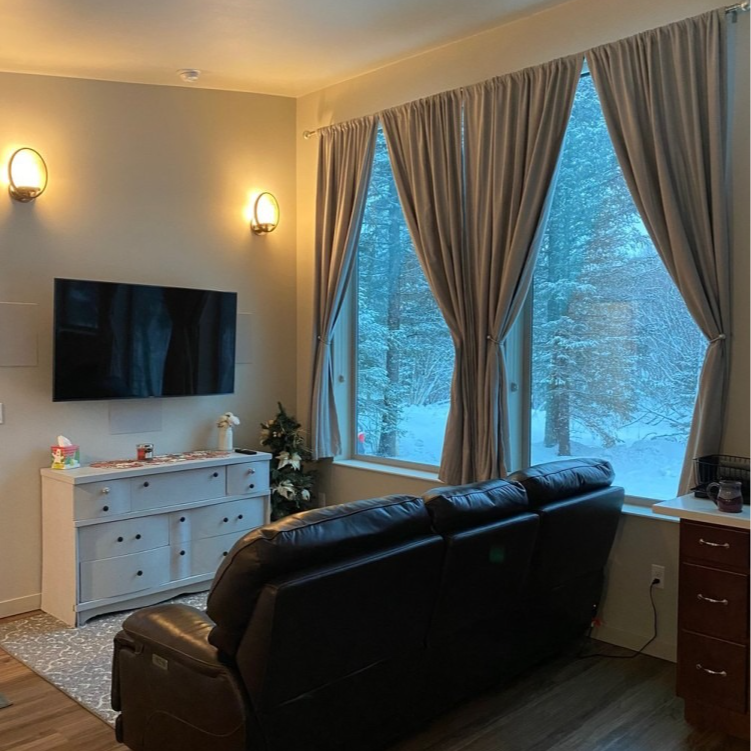 Living room with a snow-covered view through large windows, brown leather recliner, and TV above a white dresser.