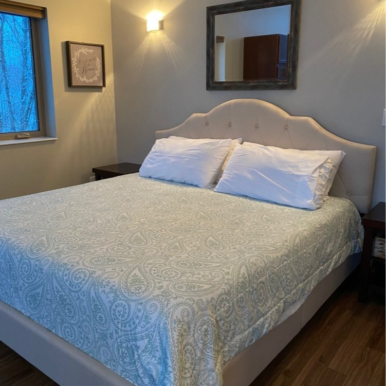 Bedroom with a bed, white bedding, and a light blue patterned cover. A mirror and art hang above.
