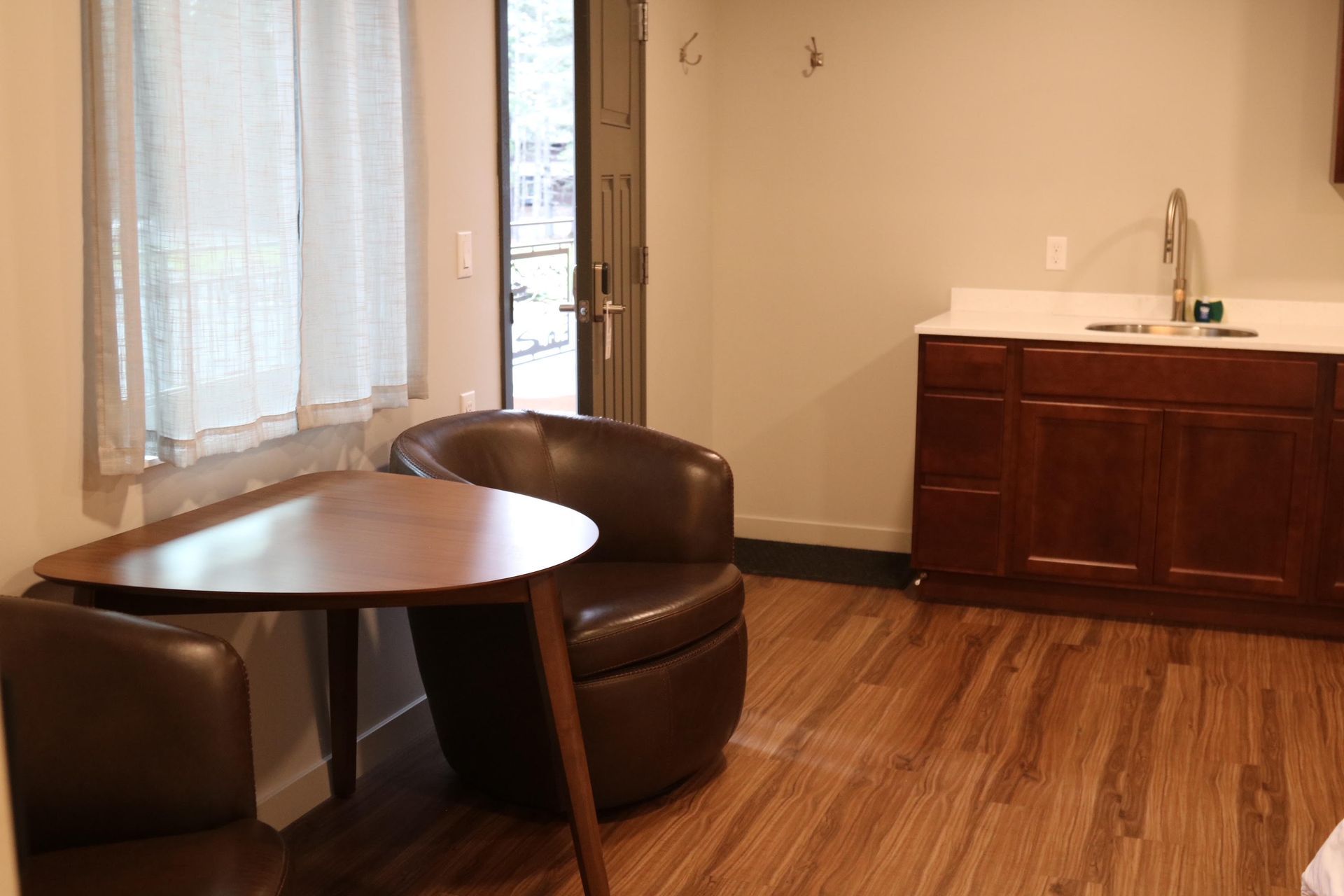 Small room with wooden floor, table and chairs, and a kitchenette.