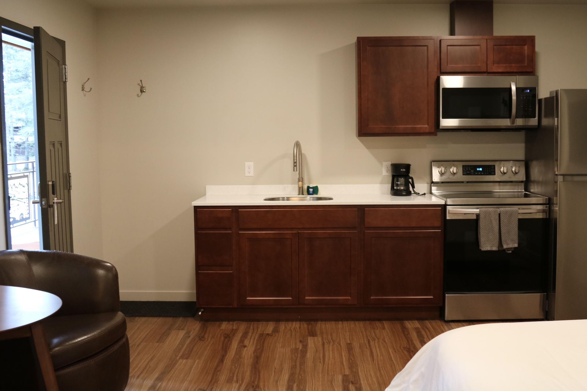 Small kitchen area with cabinets, microwave, stove, sink, and refrigerator. Brown cabinets and wood floor.
