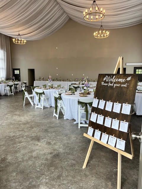 Wedding reception hall with tables, chairs, decorations, and a seating chart on an easel.