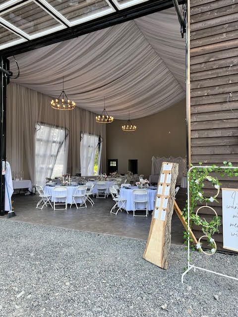 Indoor event venue with round tables, draped ceiling, and chandeliers, visible from the gravel exterior.