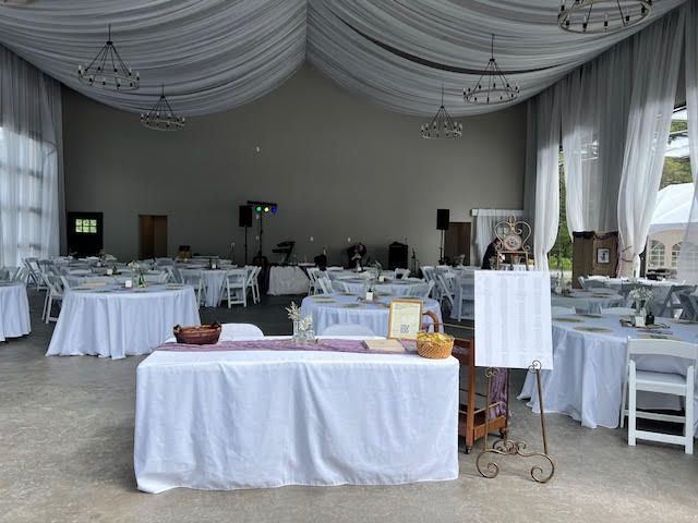 Wedding reception hall with draped ceiling, white tables, and chairs.