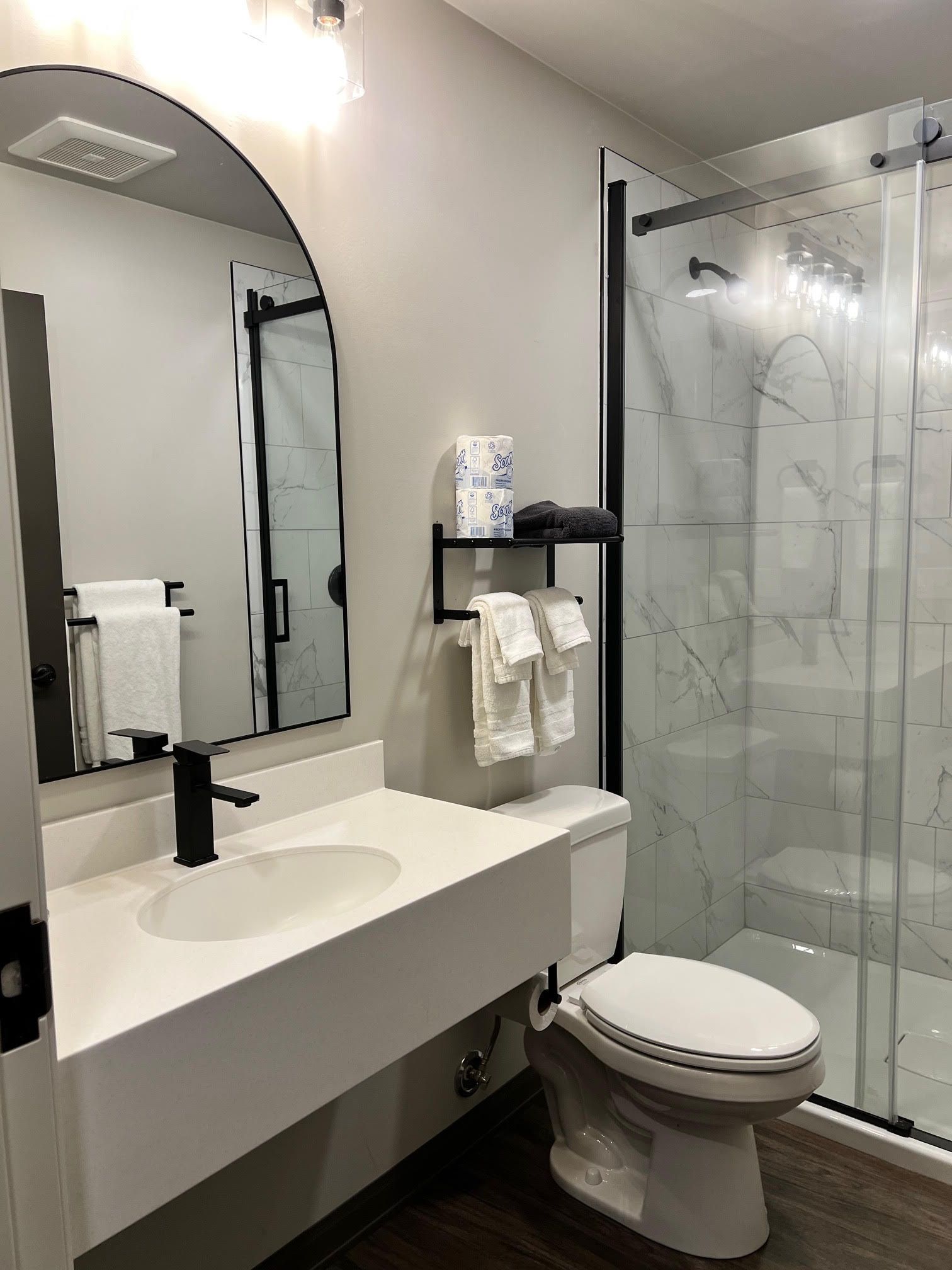 Modern bathroom with white sink, toilet, and shower with marble tile. Black accents.