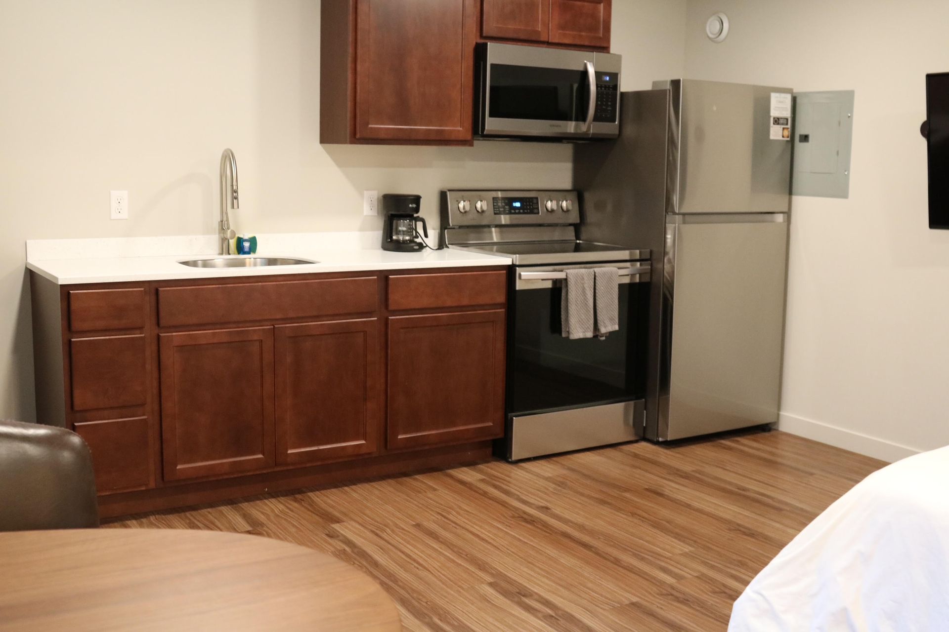 Kitchenette with brown cabinets, white countertop, stainless steel appliances, and wood floor.