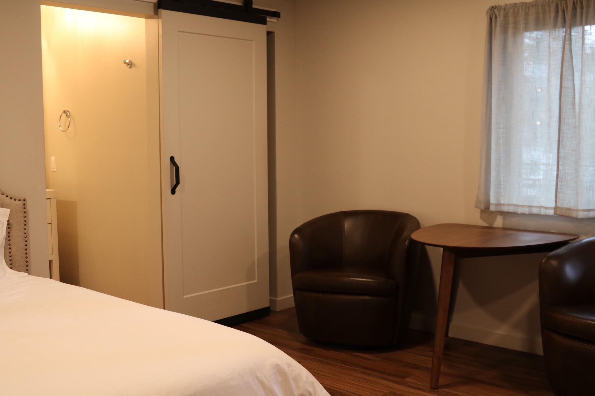 Bedroom with a white sliding door closet, two brown chairs, and a small table by a window.