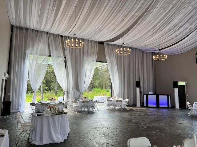 Wedding reception hall with draped white fabric, tables, and chandeliers.