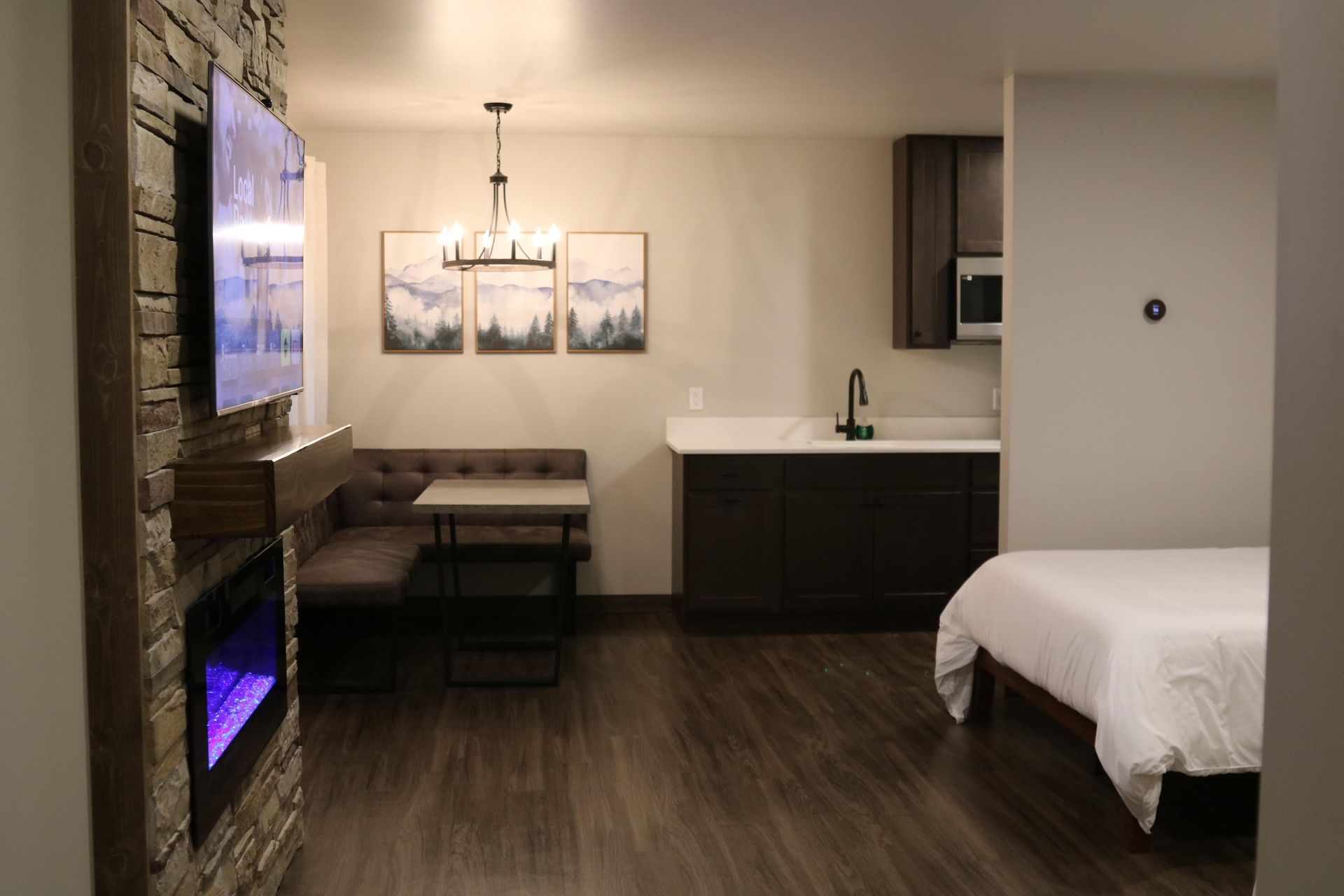 Cozy studio apartment with fireplace, kitchenette, dining nook, and bed, illuminated by a chandelier.