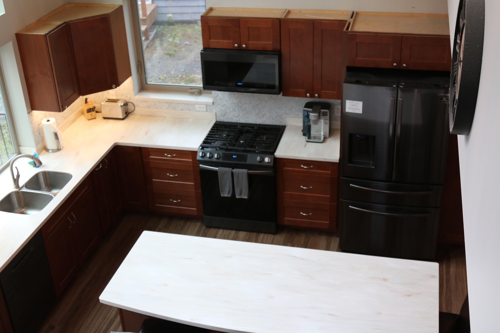 High-angle view of a kitchen with dark cabinetry, white countertops, black appliances, and a white island.