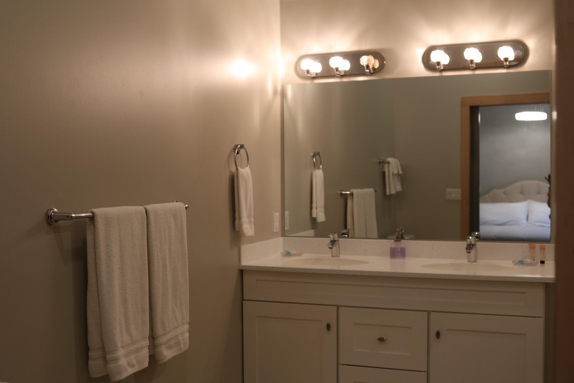 Bathroom with double sinks, white vanity, large mirror, and three-bulb light fixtures.