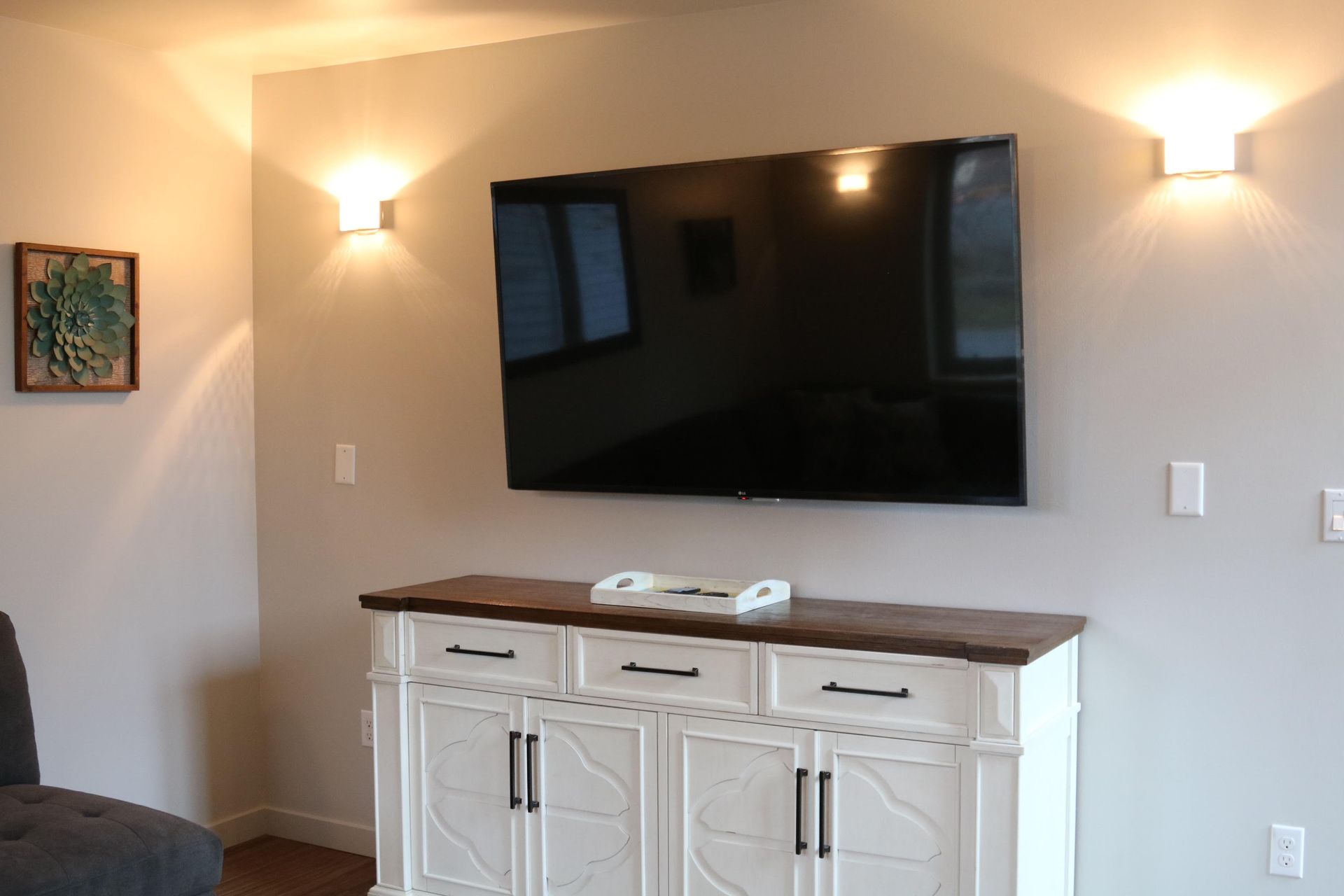 TV above white cabinet with two sconces. Small framed artwork on the left.