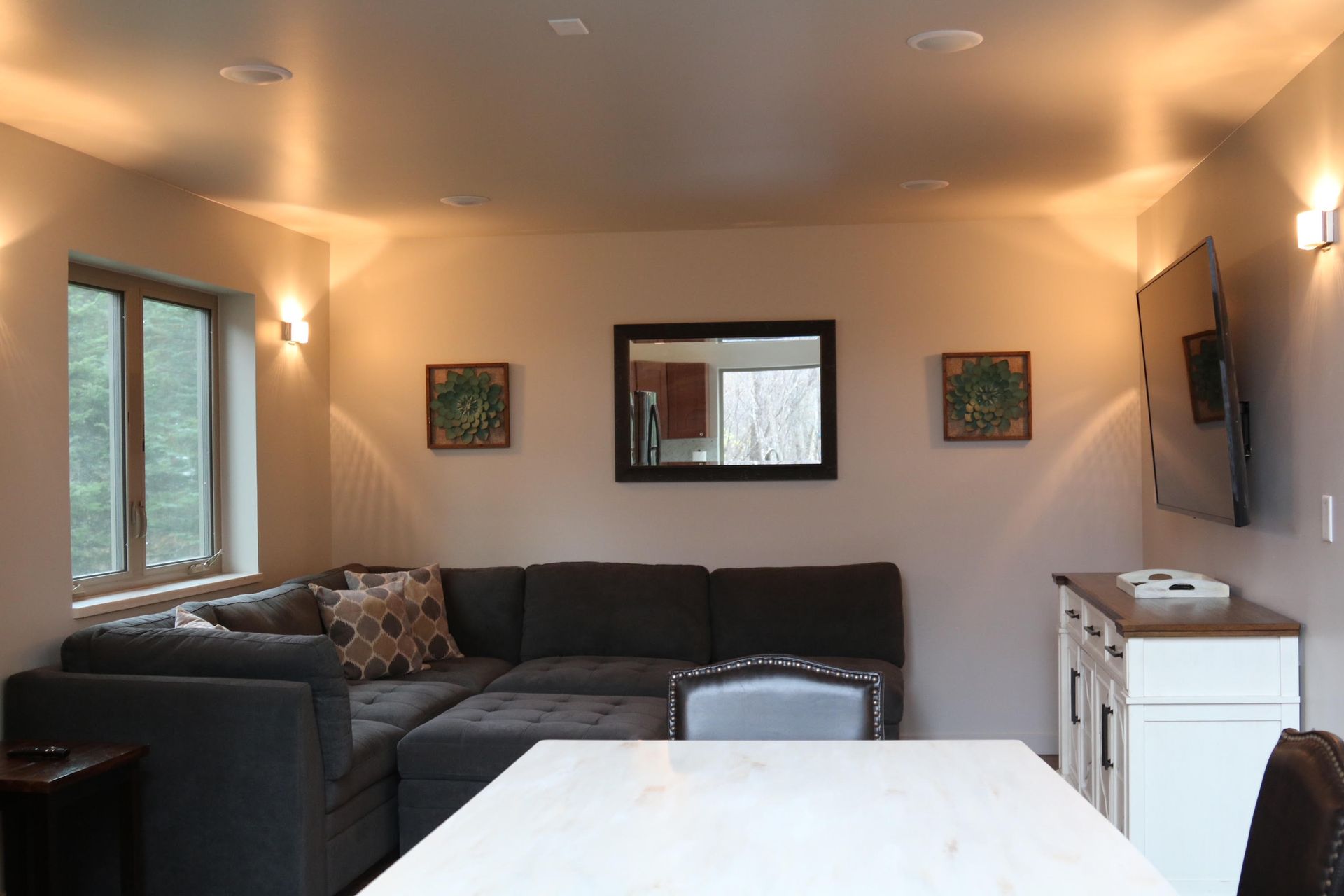 Living room with sectional sofa, dining table, mounted TV, and window.