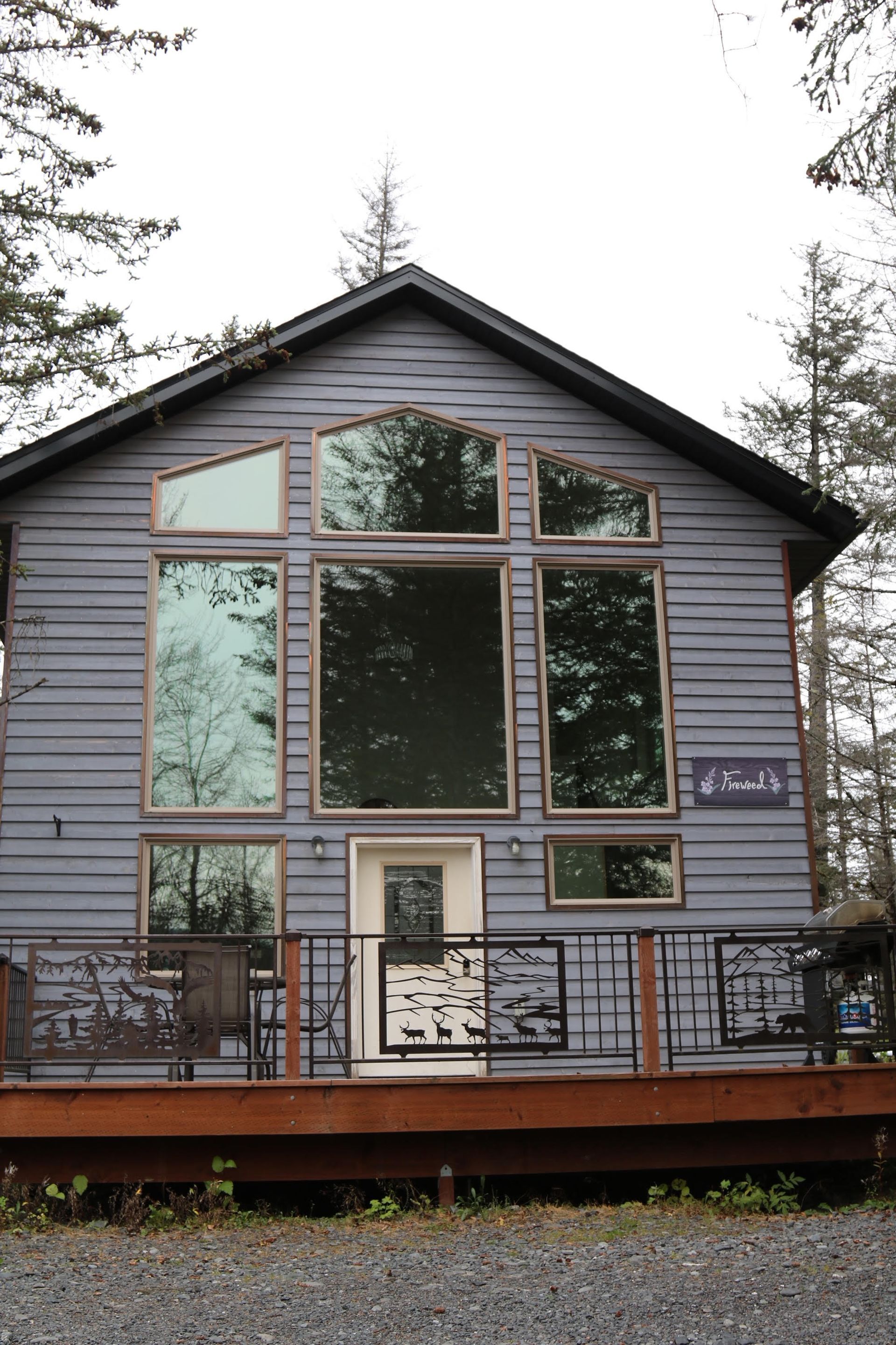 Gray cabin with large windows and a small deck, set among trees.