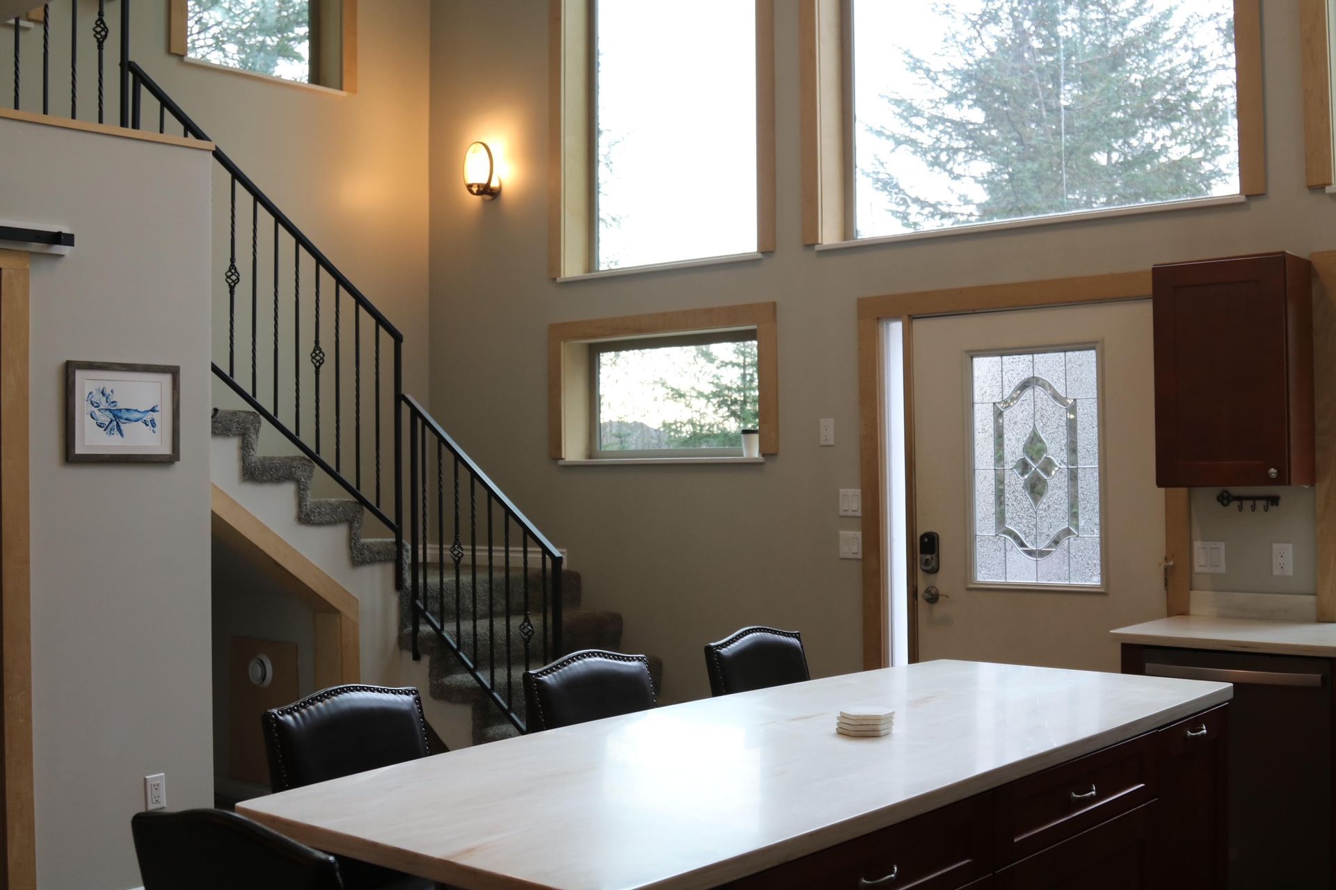 Interior with staircase, kitchen island, windows, and front door. Brown cabinets and light gray walls.