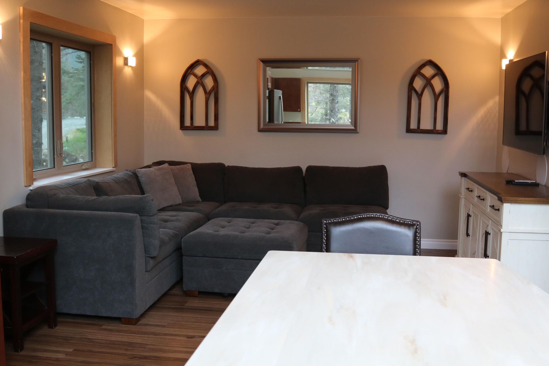 Living room with sectional sofa, decorative arches, mirror, TV, and light-colored kitchen island.