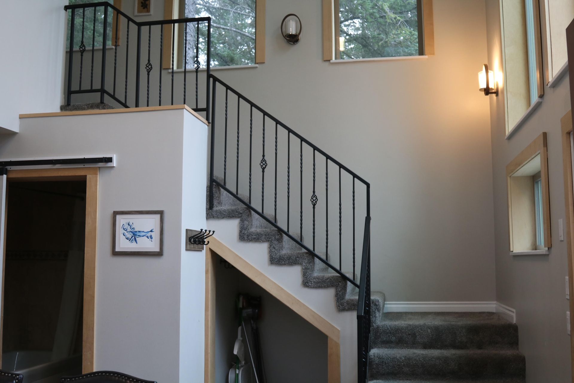 Staircase with black railing and light gray walls. Beige trim frames stairs and windows.