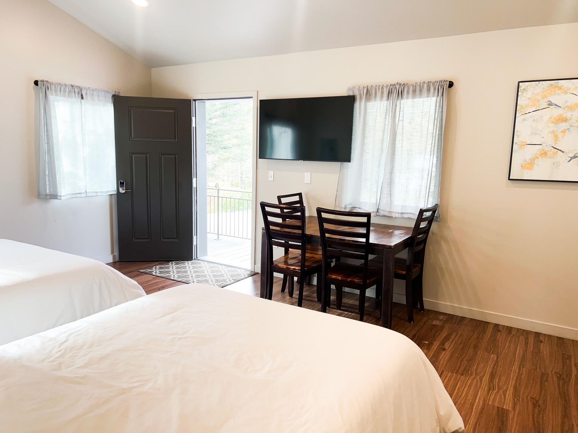 A hotel room with two beds, a small dining table, TV, and an open door to a patio.