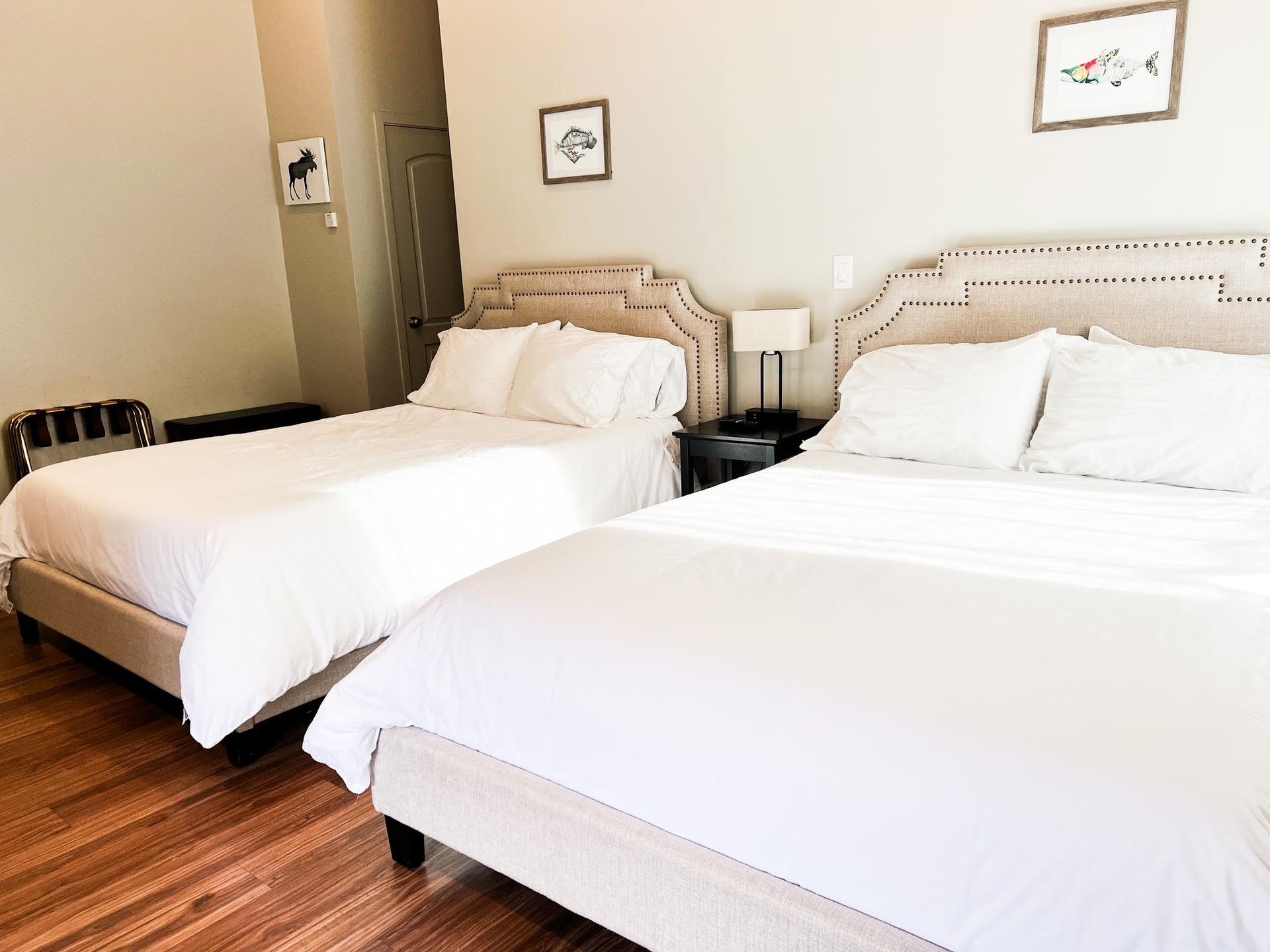 Two beds with white bedding in a hotel room with light walls and wooden floors.