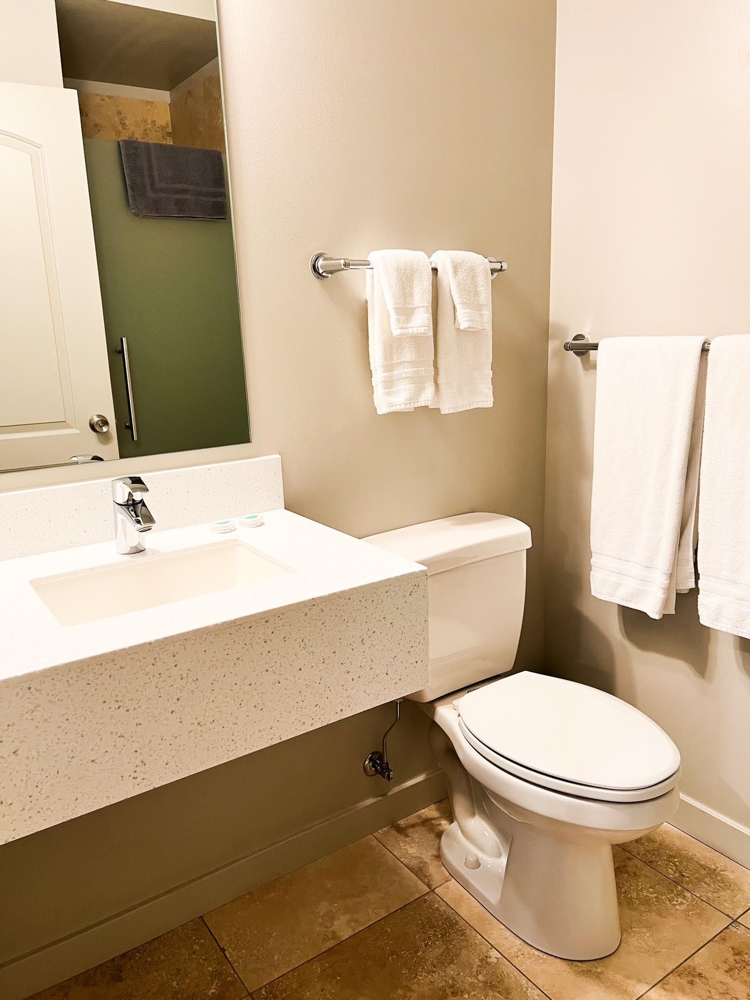 Bathroom with white sink, toilet, and towels, beige walls, and brown tile floor.