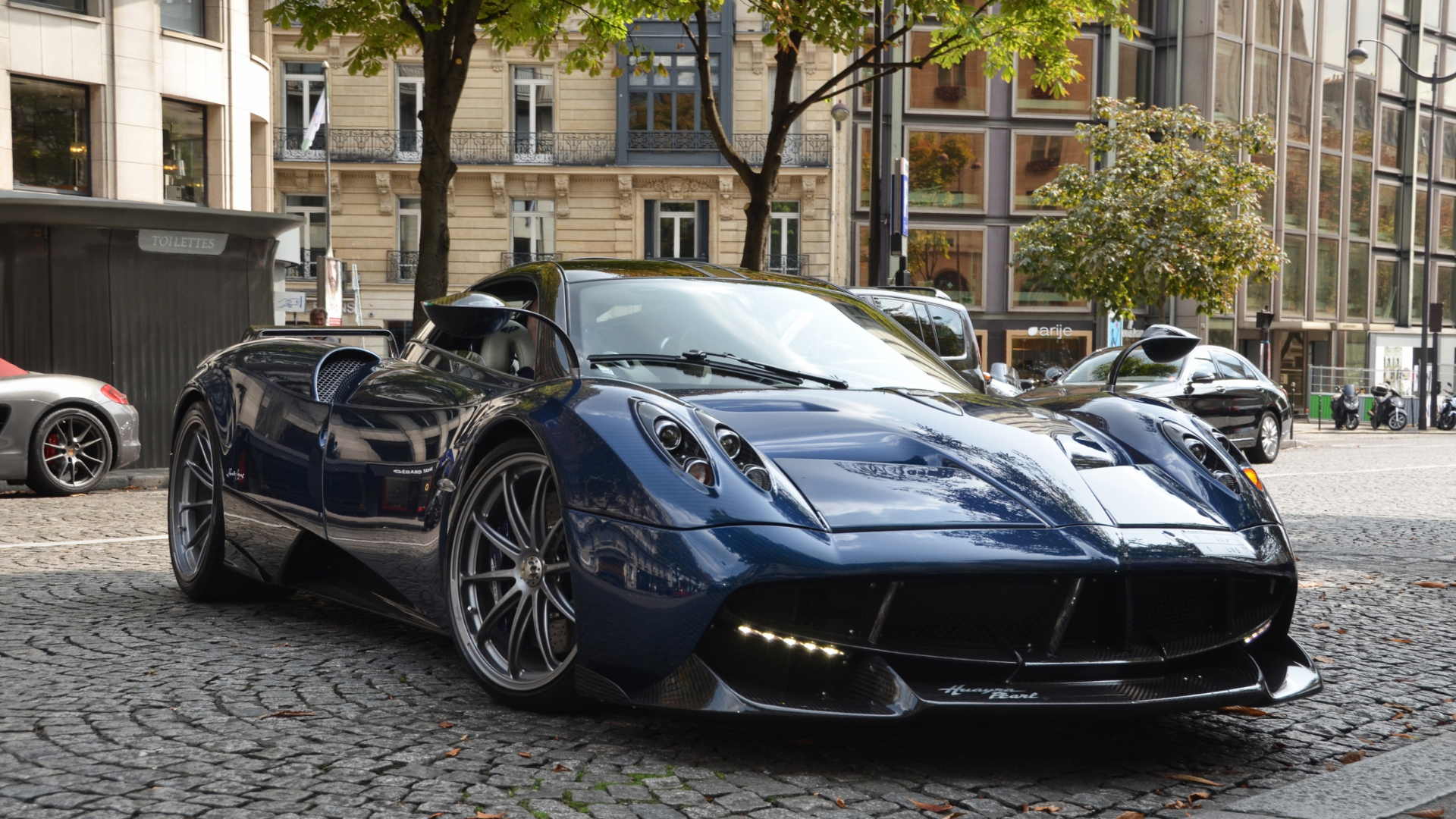 A blue sports car is parked on a cobblestone street in front of a building.