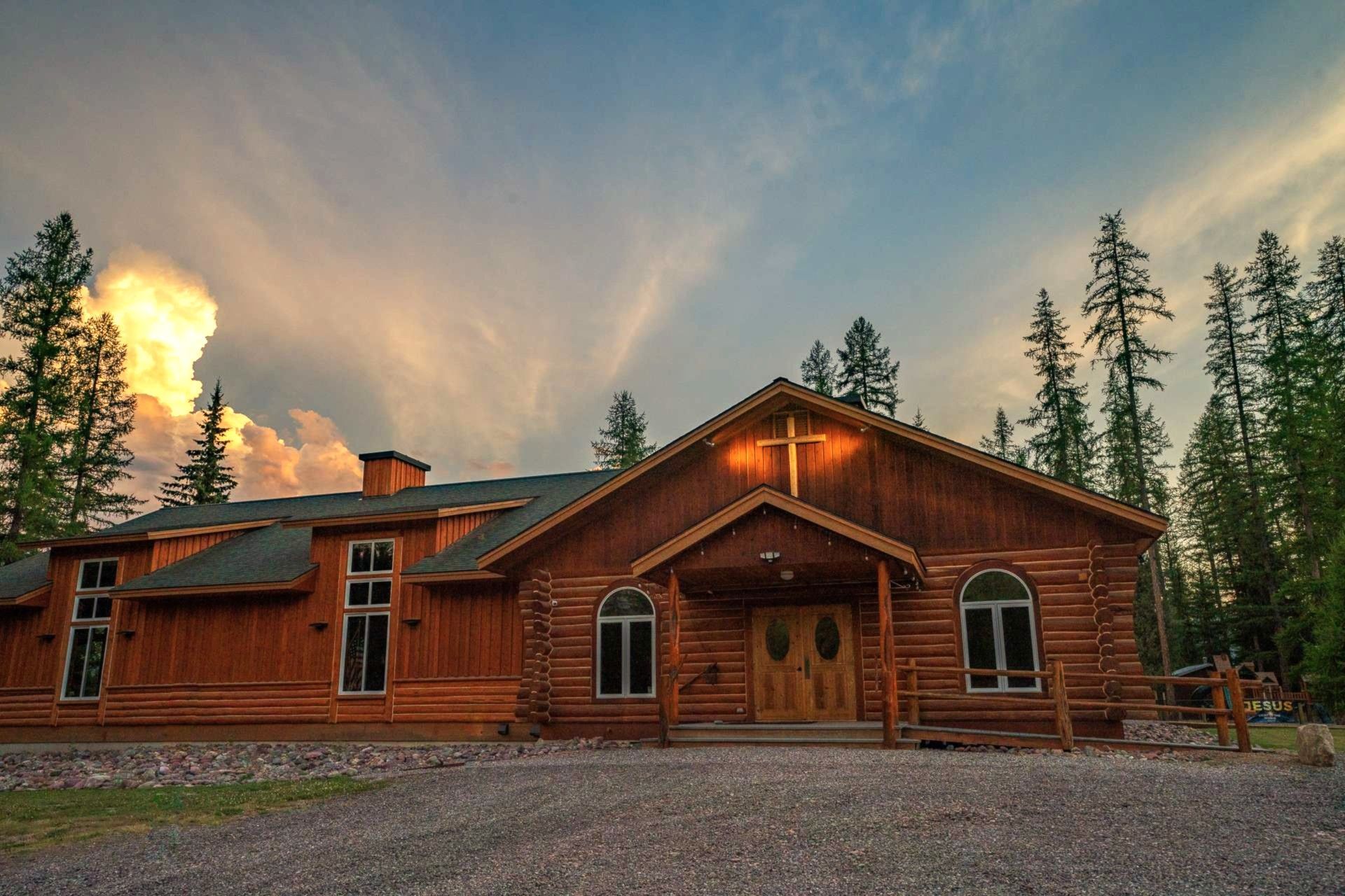 Wooden church with cross on the roof, set against a cloudy sunset sky.
