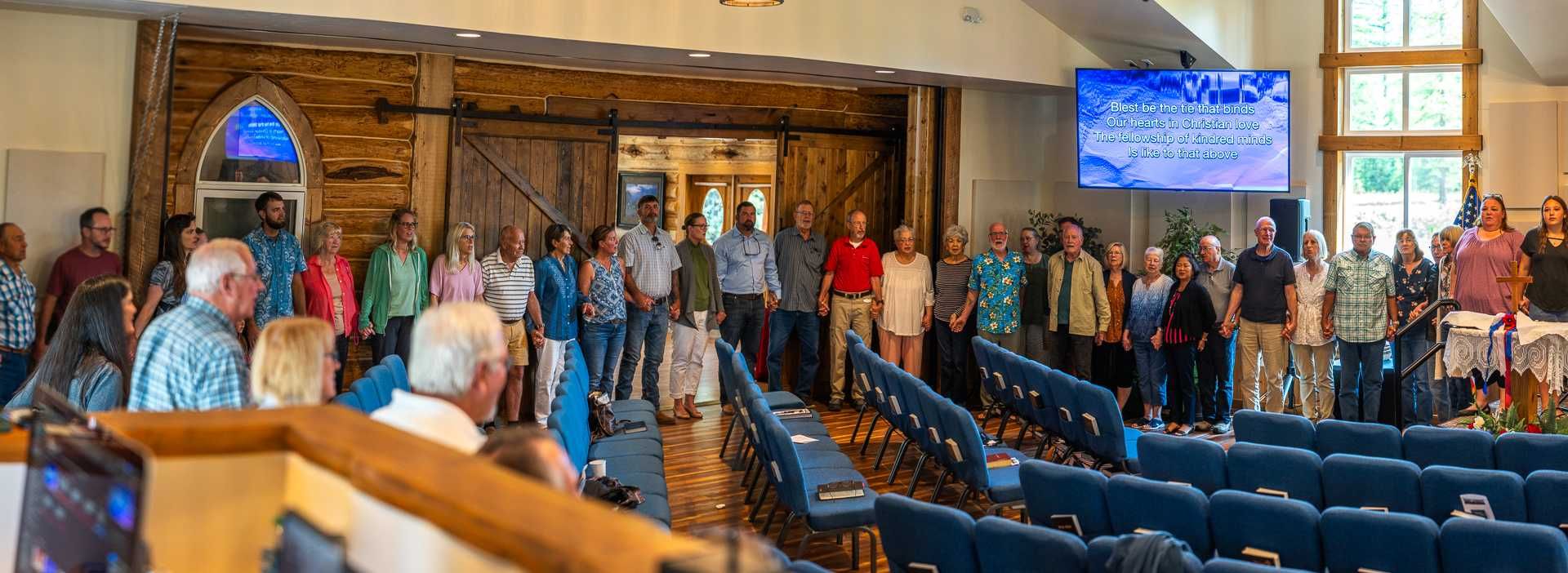Group of people standing in a church, some facing the camera. Church setting with blue pews, wooden doors.