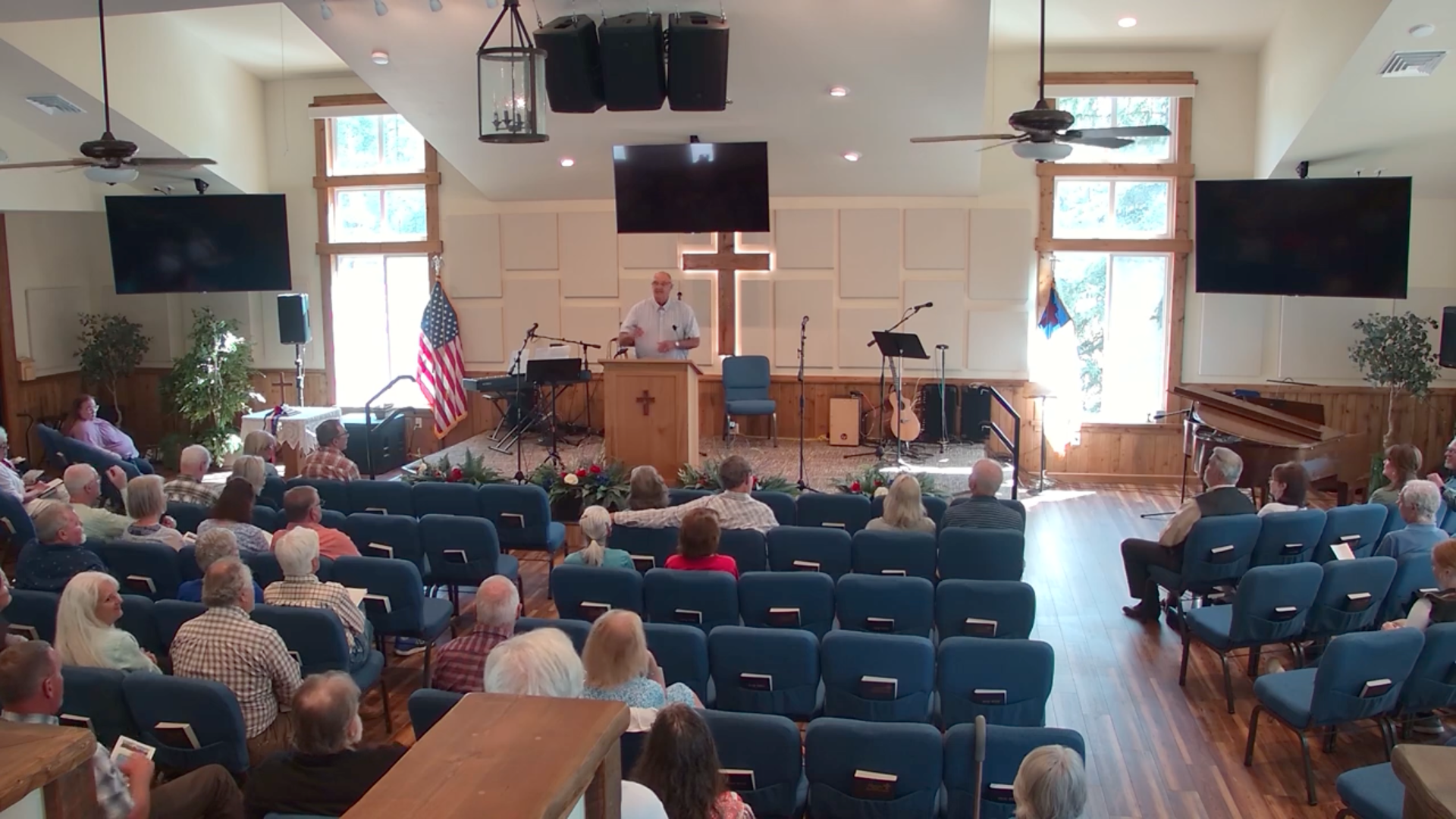 A church service with a preacher speaking, an audience, and a wooden cross.
