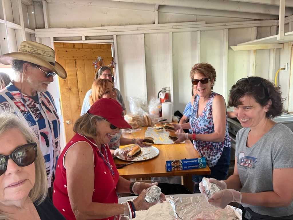 People preparing food at a cookout inside a white wooden structure.