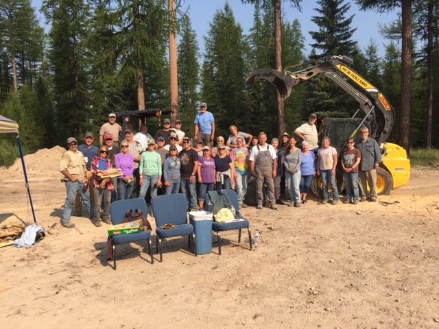 Group of people standing in a wooded area near construction equipment, posing for a photo.