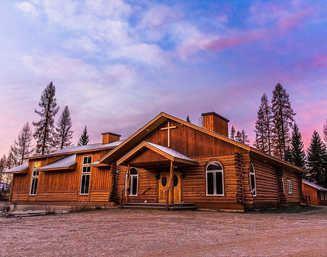 Rustic wooden church with cross, under a sunset sky, snow on the ground.
