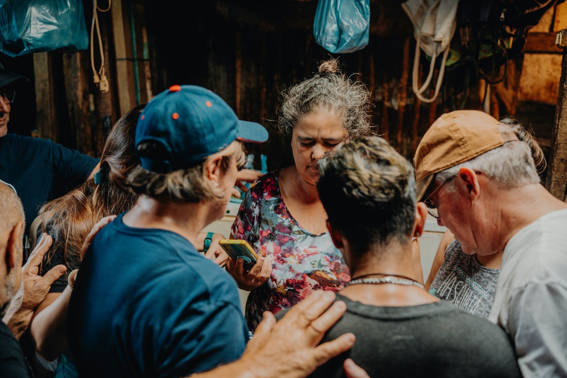 A group of people gathered closely together, some looking at a phone, in a dimly lit space.