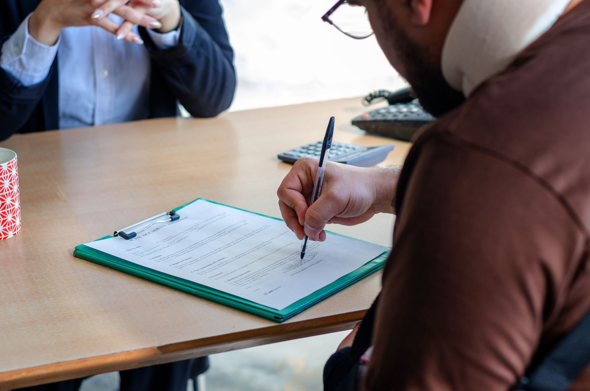 Client signing legal paperwork on a clipboard during a consultation with an attorney at a desk Client signing legal paperwork on a clipboard during a consultation with an attorney at a desk
