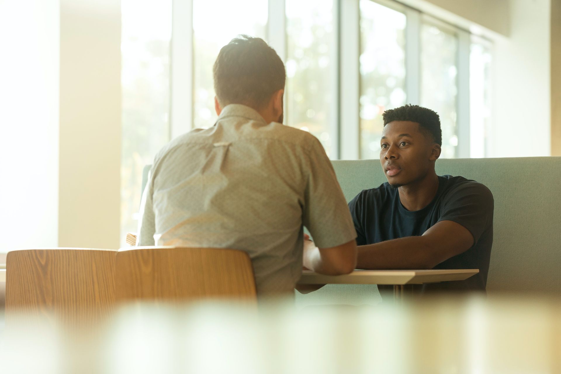 A young black man and young white man sit facing each other at a table is calm conversation