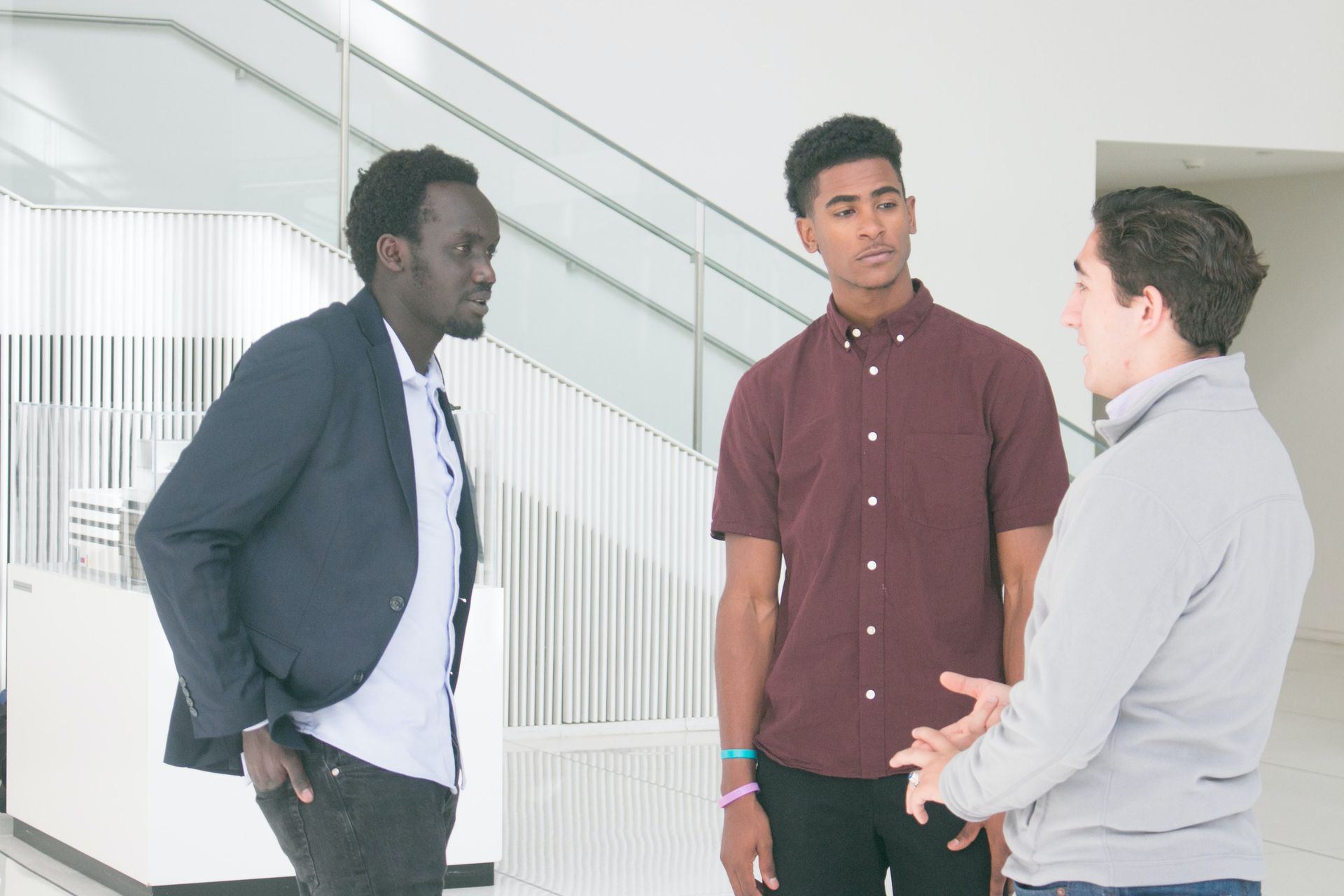 Two Black men and a white man are standing in a white stairwell conversing