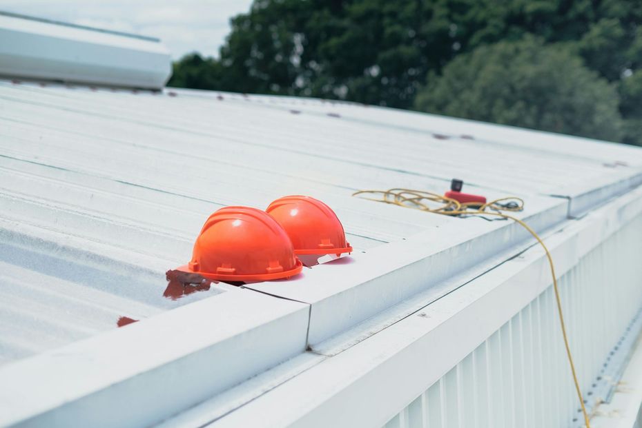Two orange hard hats sit on a white metal roof next to a coiled yellow rope.