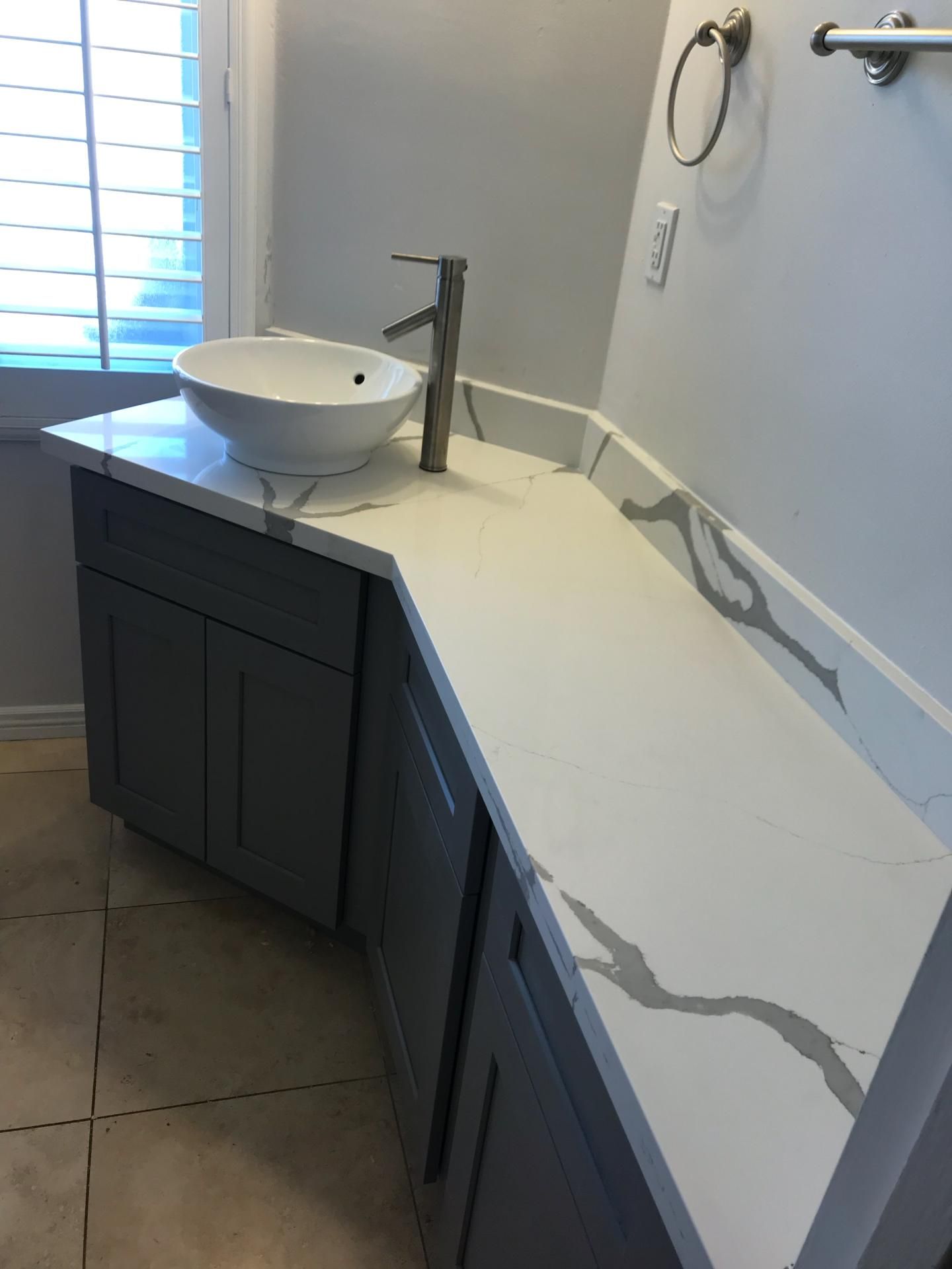 A bathroom with a sink , cabinets , and a window.