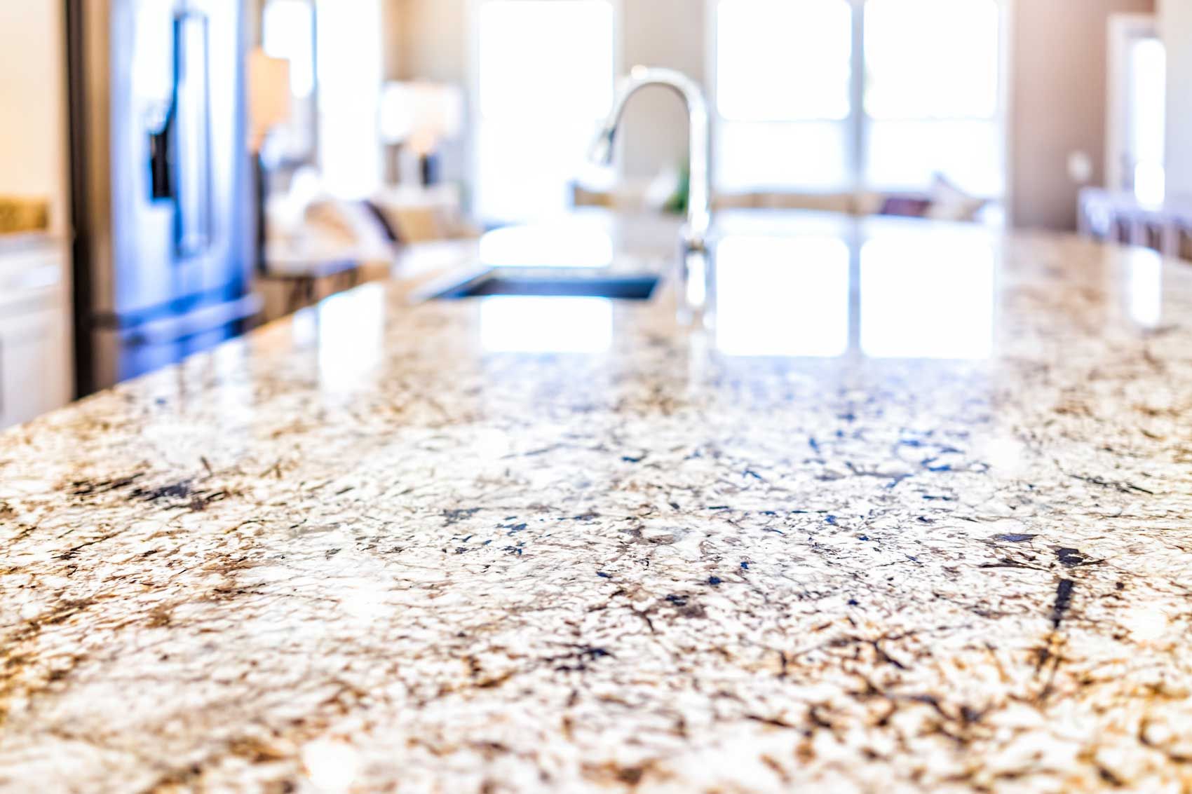 A close up of a granite counter top in a kitchen with a sink and refrigerator.