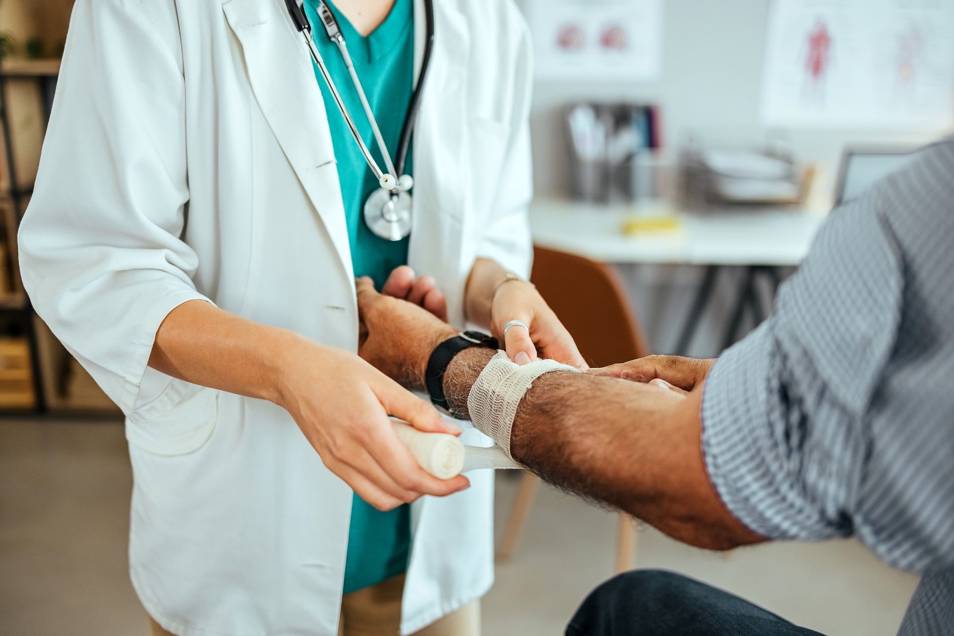 Doctor wrapping bandage around patient's arm in a medical office setting.
