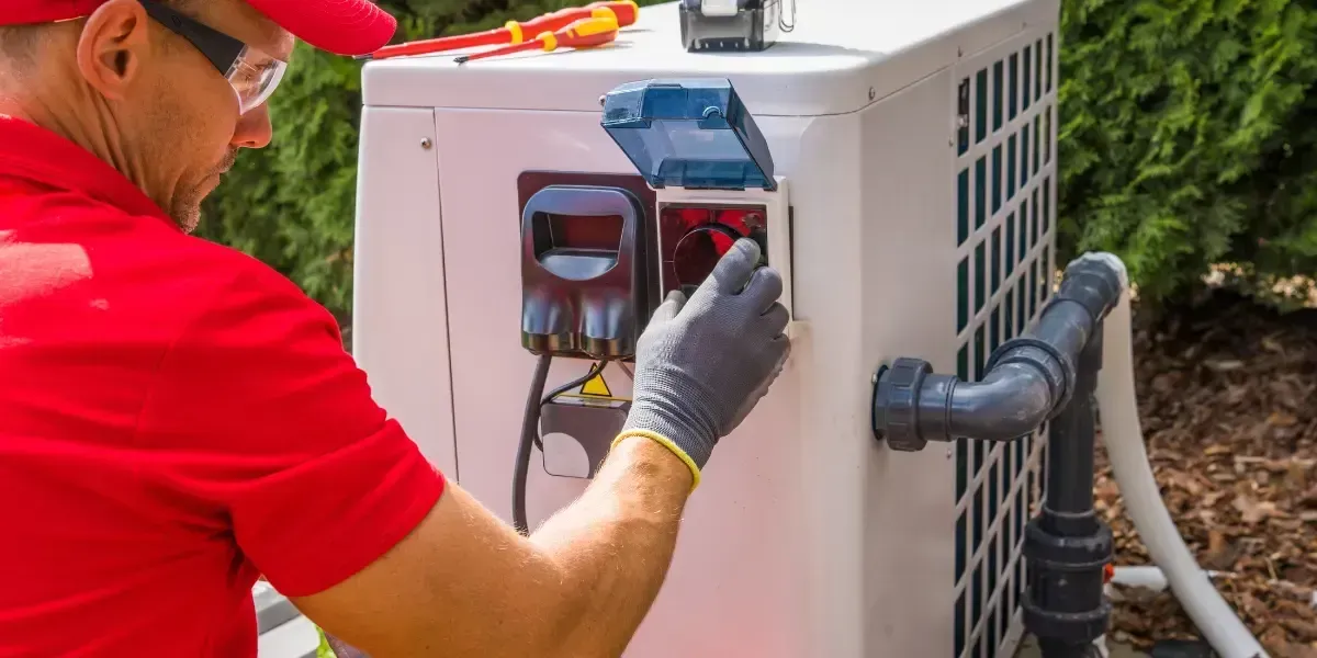 Electrician in red shirt and cap works on outdoor unit.