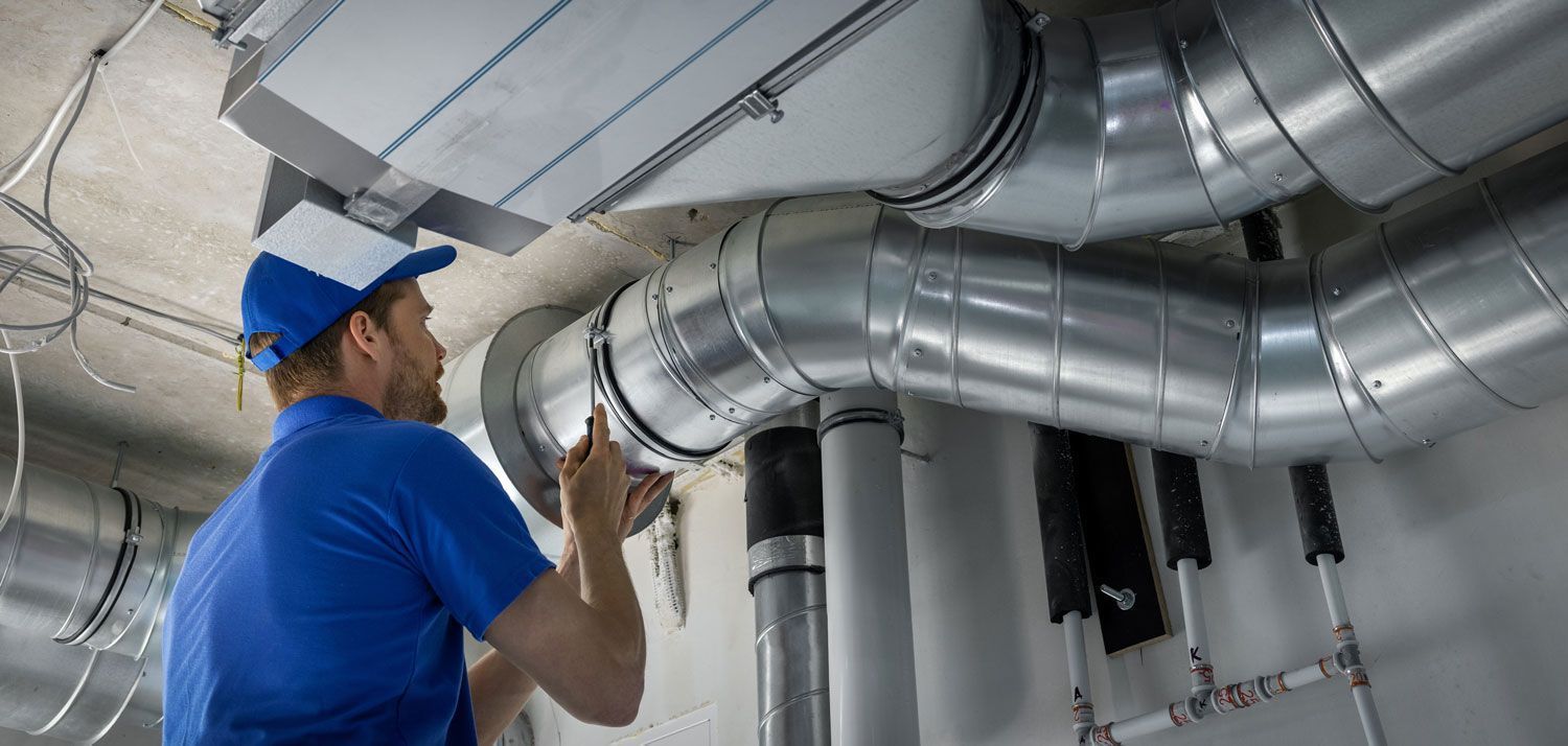 A person in a blue uniform working on ventilation pipes in a building.