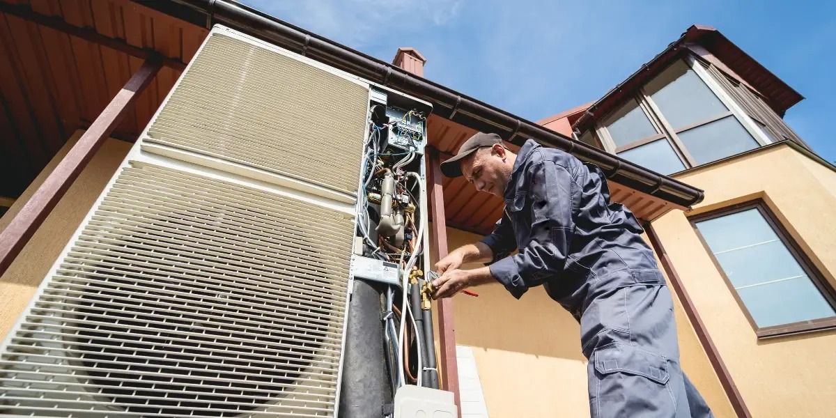 A technician repairs an outdoor AC unit attached to a house.