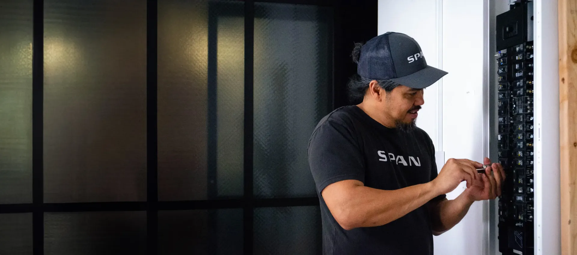 Man in cap working on a circuit breaker panel.