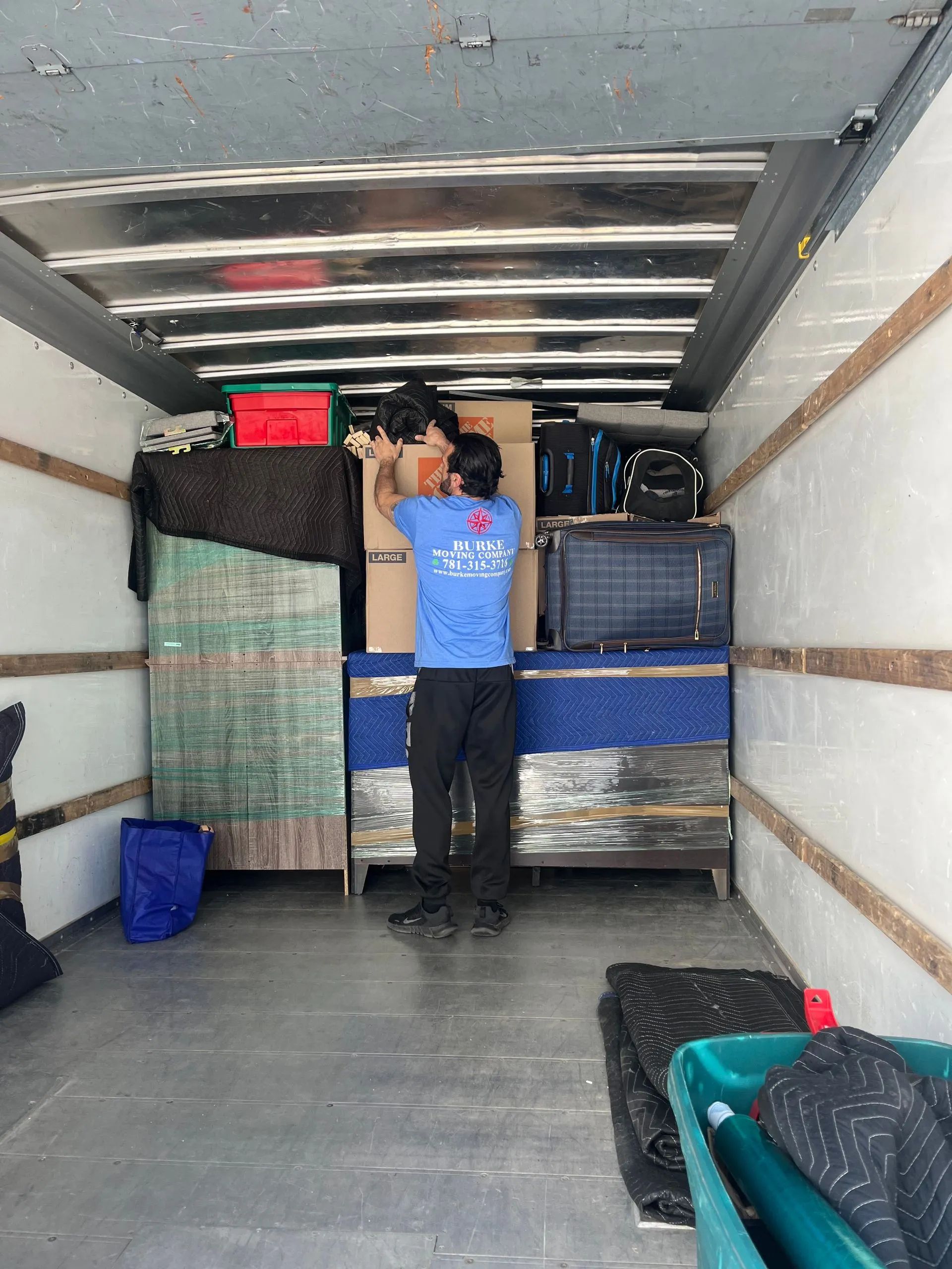 Man loading items into the back of a moving truck. Interior view with various boxes and furniture.