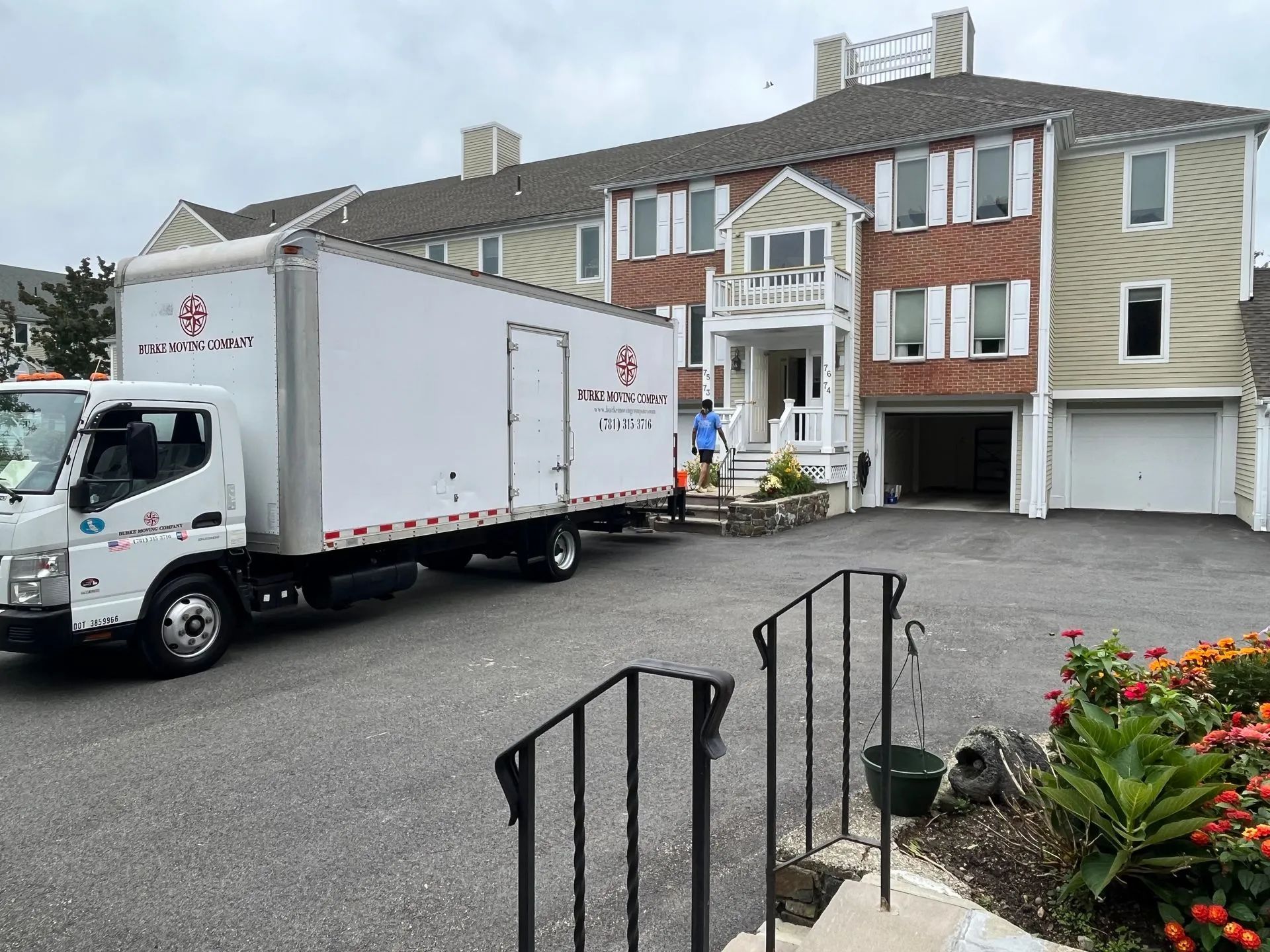 Moving truck parked in front of a multi-story house. A person stands near the house.